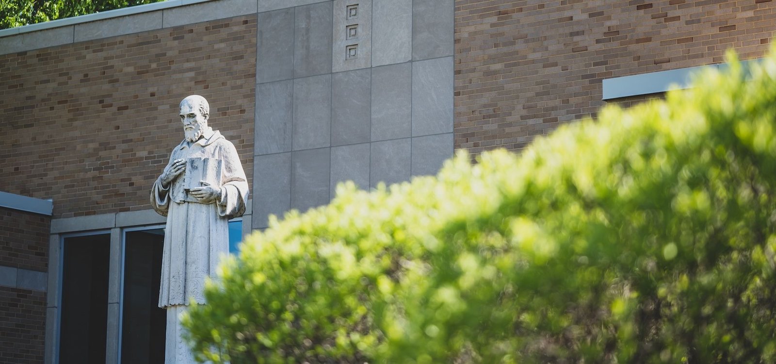 Statue of St. Francis de Sales beside the hedges at the front of Salesianum School