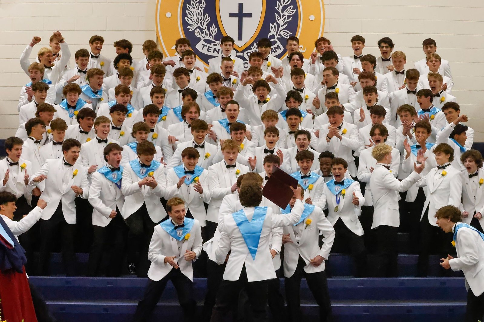 Rows of Salesianum students in white jackets gathered on stage under the crest